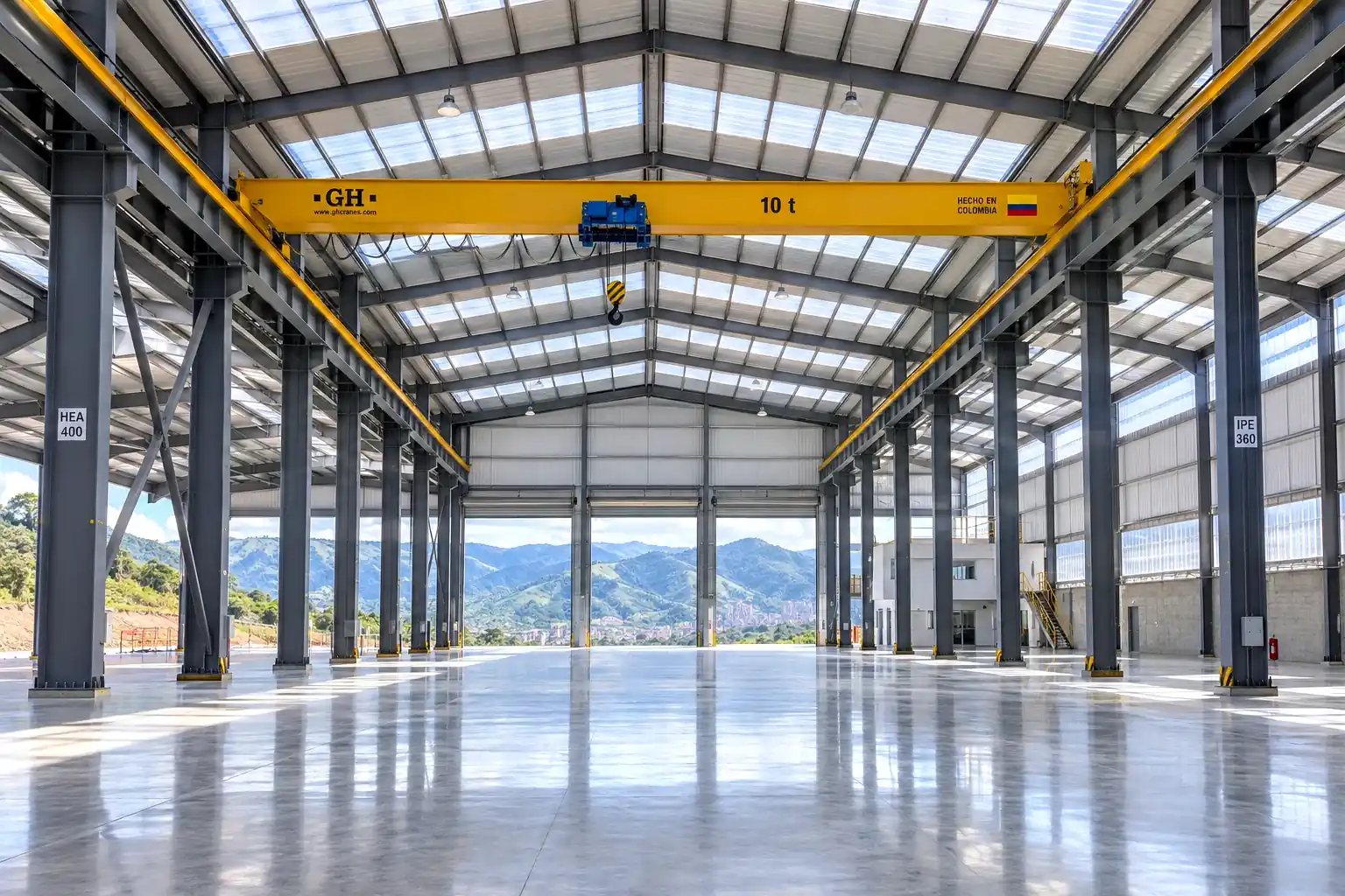 Interior de nave industrial moderna con pórticos HEA/IPE, puente grúa amarillo y cordillera de Antioquia al fondo, Medellín